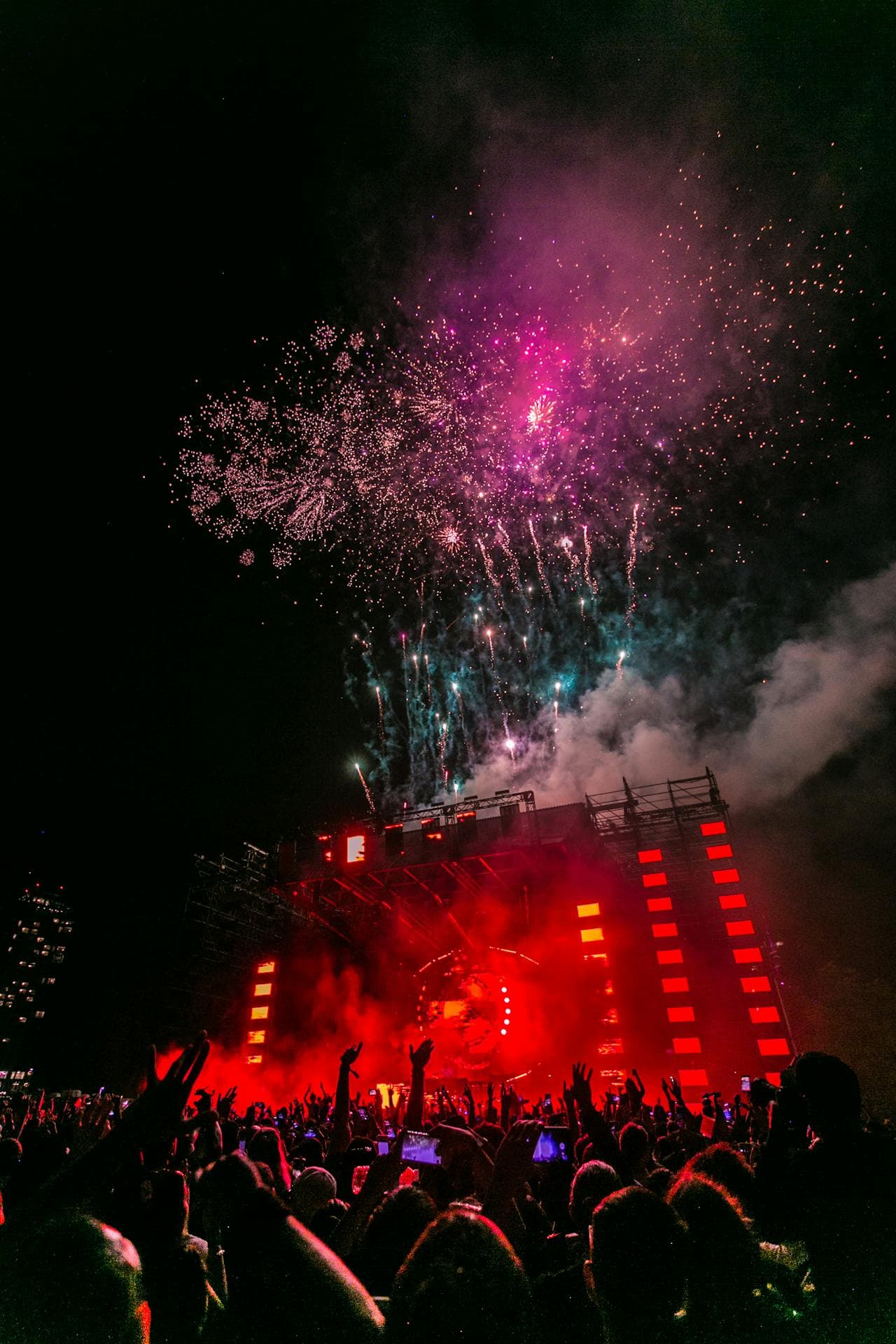 Concert crowd lit by red stage lights and fireworks